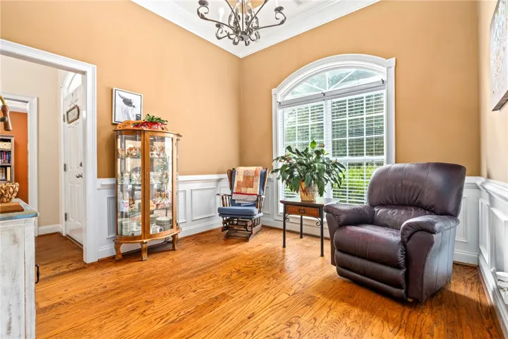 Hardwood floors and wainscoting frame this inviting living area, illuminated by a large arched window.