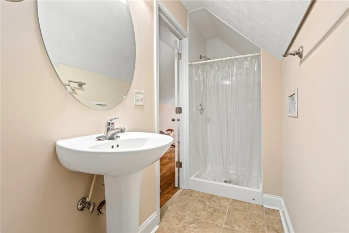 A well-appointed bath features a shower and pedestal sink, all under an angled ceiling.