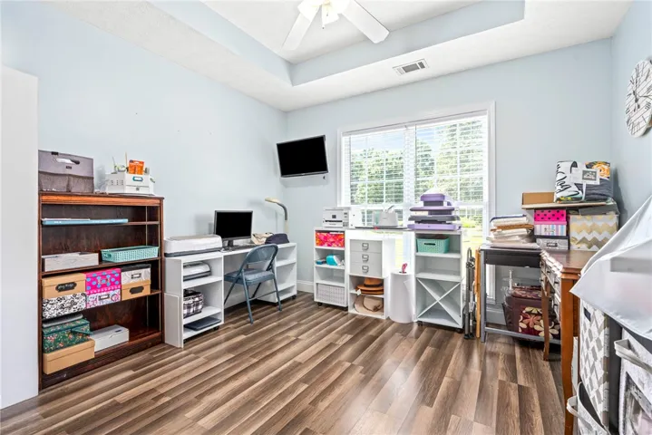 A well-lit study with tray ceilings and wood flooring provides a versatile space.