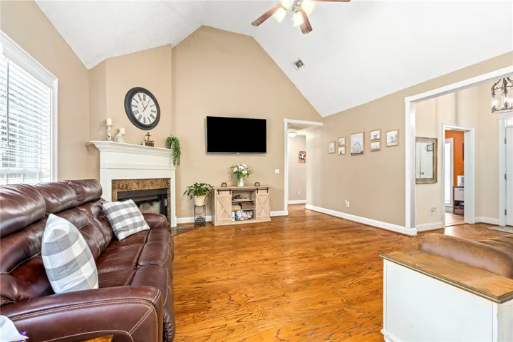 A spacious living room features vaulted ceilings, rich hardwood floors, and a welcoming fireplace with a classic mantel.