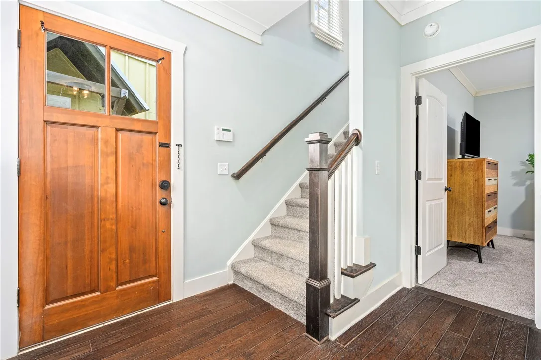 A welcoming entry features rich wood flooring, a matching front door, and a carpeted staircase leading to upper levels.