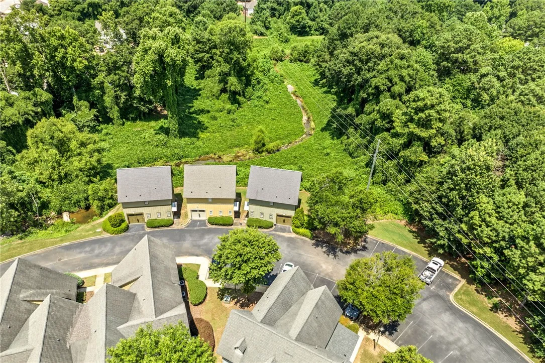 Aerial view showcasing townhomes nestled beside a tranquil wooded area and a winding stream.