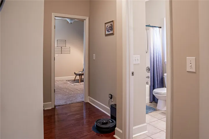 Rich hardwood flooring guides visitors from the central hallway into a well-appointed bathroom and secondary room.