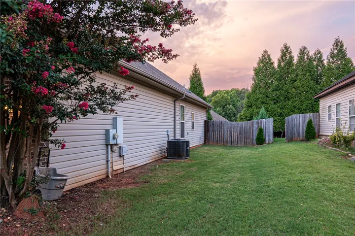 A vibrant crape myrtle blossoms against the neutral siding of a well-maintained home with a private, fenced yard.