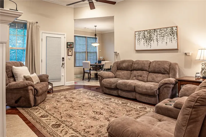 A comfortable living space featuring hardwood flooring and a stylish ceiling fan, opening into a bright dining area.