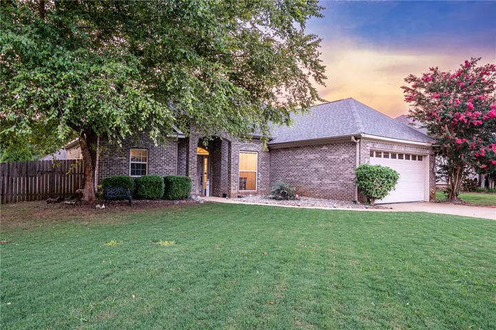 Mature trees frame this traditional brick home with an attached garage and well-maintained front yard.