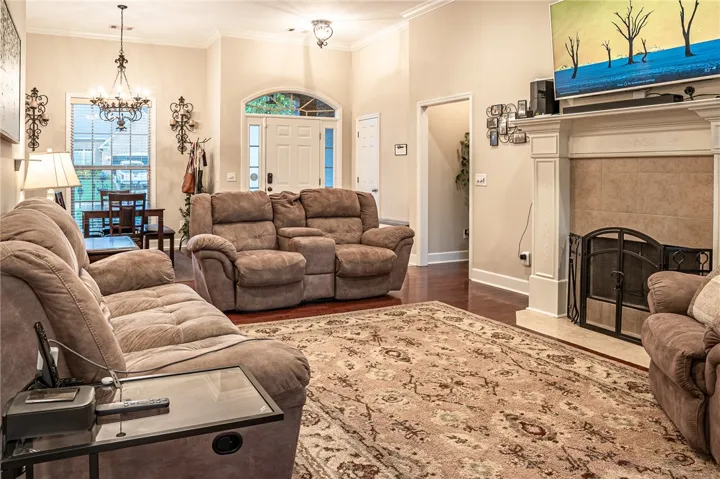 A welcoming living area boasts high ceilings, a grand fireplace, and polished hardwood floors leading to the front entry.