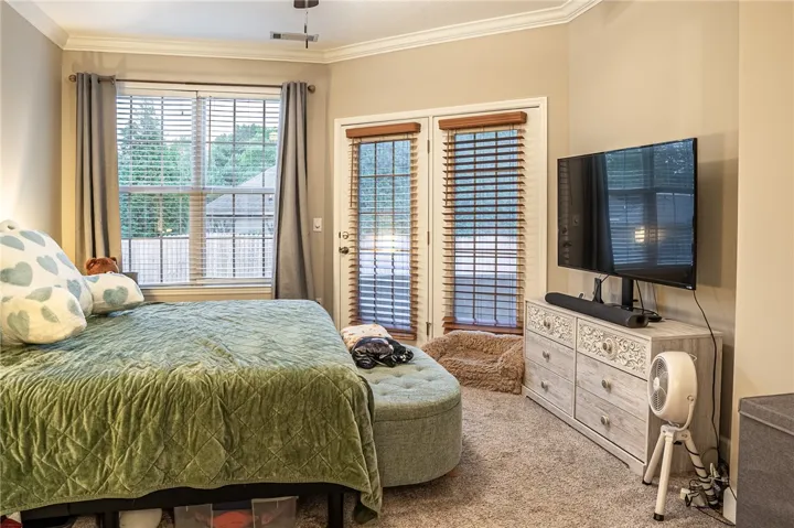 Natural light filters into this carpeted bedroom through a large window and double glass-paneled doors.