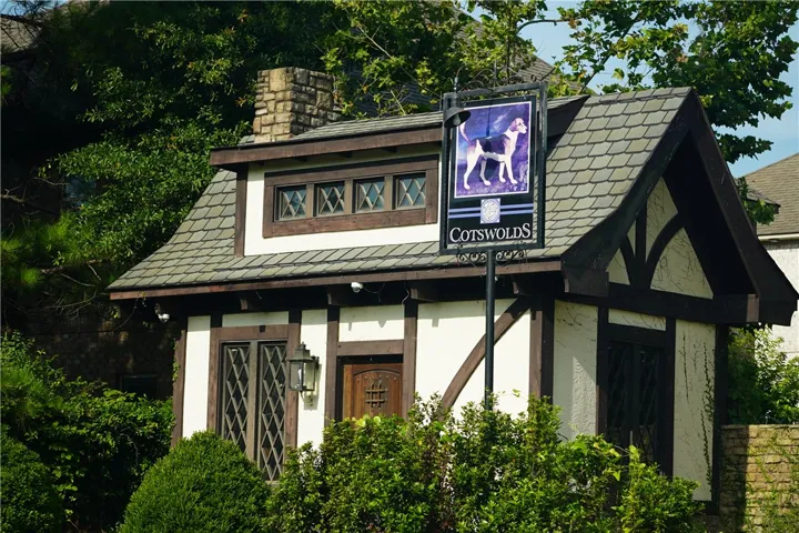 A storybook exterior boasts intricate Tudor-style architecture with diamond-paned windows and a prominent stone chimney.