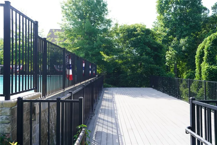 A spacious outdoor deck with sturdy fencing, ideal for entertaining by the pool and enjoying the lush green surroundings.