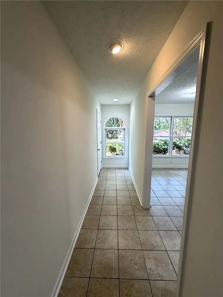 A well-lit hallway with tile flooring leads to an arched window and a bright room beyond.