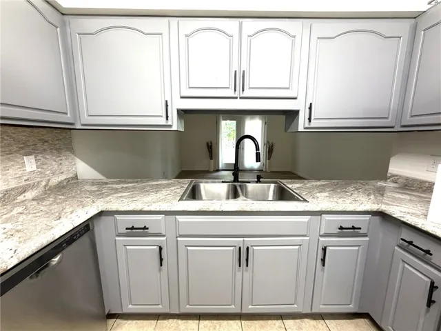 A well-appointed kitchen features ample cabinetry, stone counters, and a double basin sink.