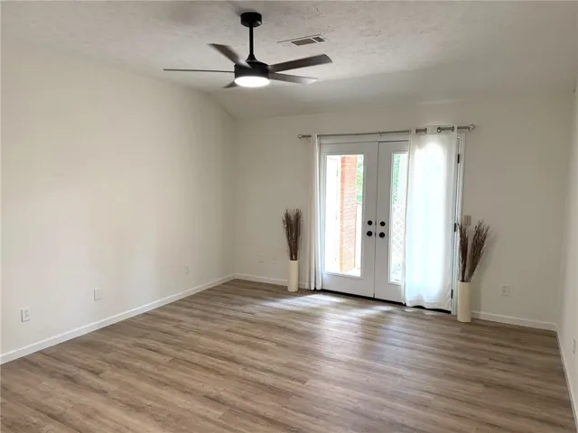 Laminate flooring extends throughout this versatile living area, complemented by a contemporary ceiling fan and elegant French doors.