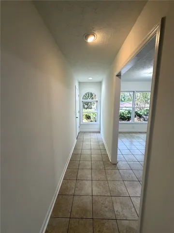 A well-lit hallway with tile flooring leads to an arched window and a bright room beyond.