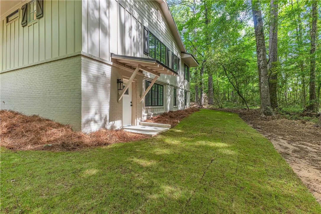 A private entry leads into a dwelling with a striking brick and board-and-batten facade, surrounded by lush, mature trees.