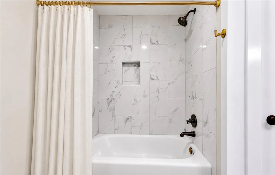 Marble-tiled shower surround with a sleek black showerhead and an integrated niche.