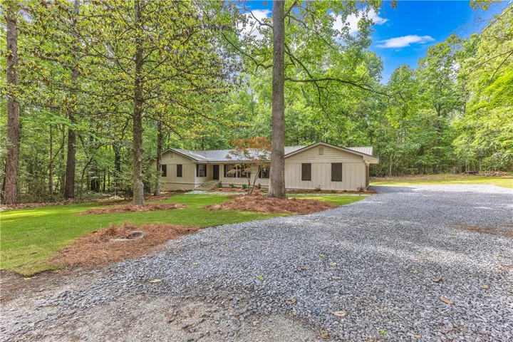 Discover a tranquil woodland retreat with a spacious gravel driveway leading to this charming, single-level home.