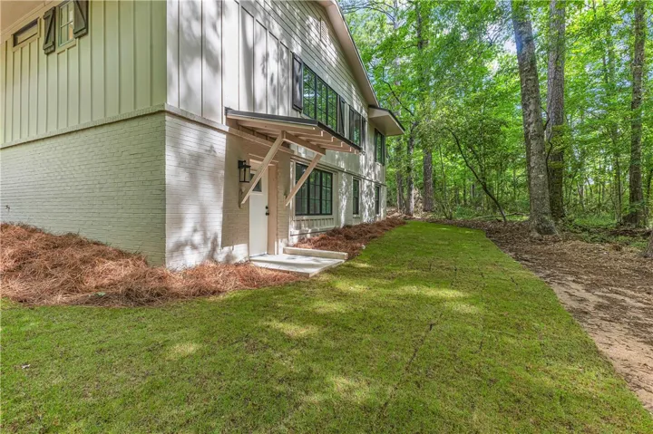 A private entry leads into a dwelling with a striking brick and board-and-batten facade, surrounded by lush, mature trees.