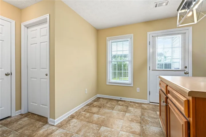 A compact kitchen area with tiled floors and ample natural light through a window and a glass-paneled door.