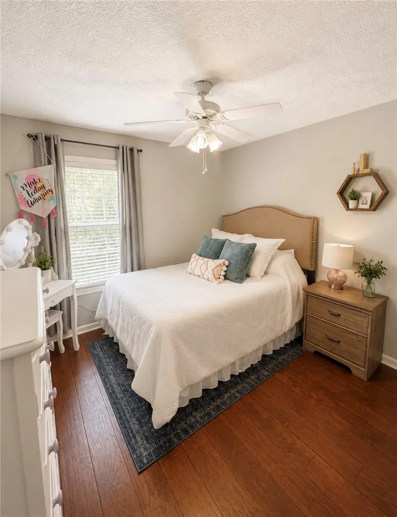 Rich hardwood floors complement a well-lit bedroom featuring a functional ceiling fan.