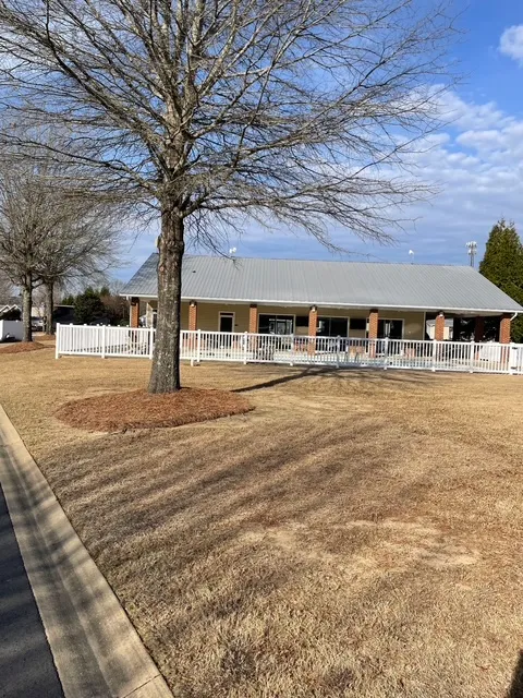 A community building with a metal roof is bordered by a crisp white fence, set against a bright sky.