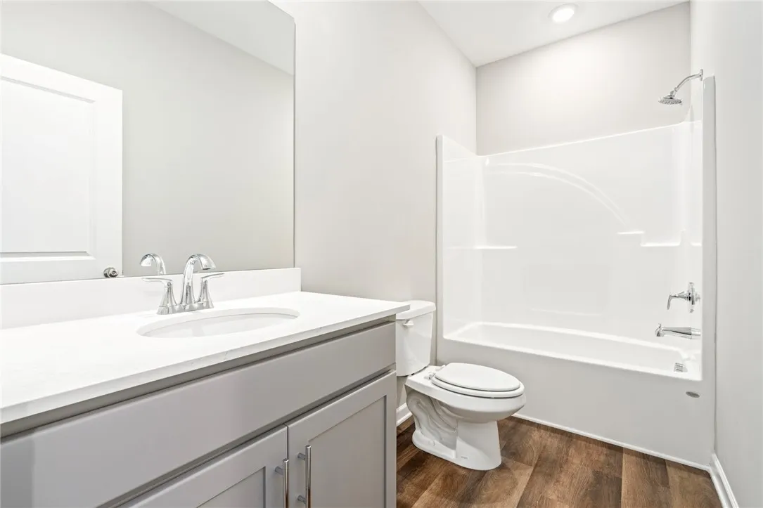 A modern bathroom features a clean white vanity top and warm wood-look flooring.