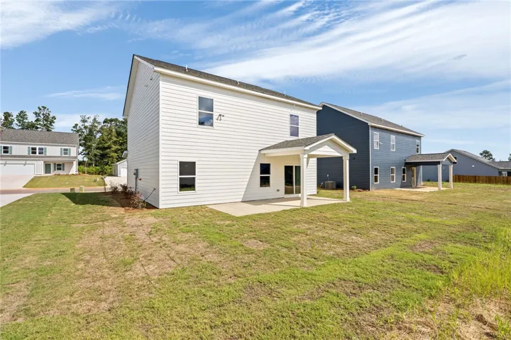 A spacious grassy yard sits behind this two-story home featuring a covered concrete patio.