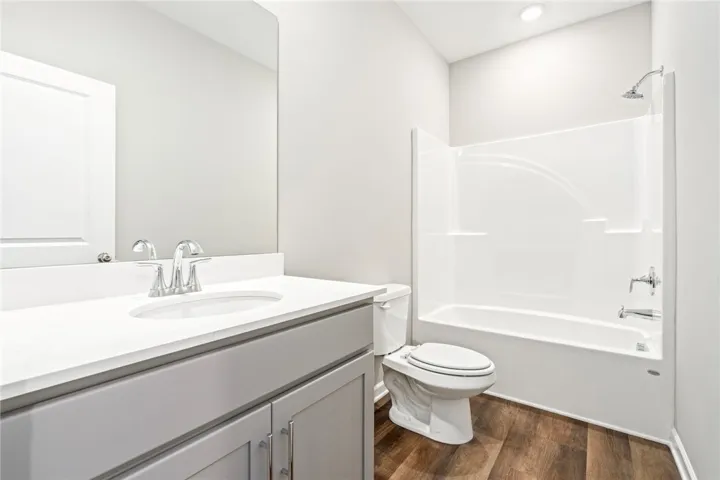 A modern bathroom features a clean white vanity top and warm wood-look flooring.