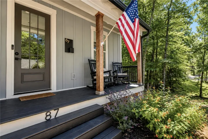 A welcoming front porch beckons with rocking chairs and vibrant surrounding foliage.
