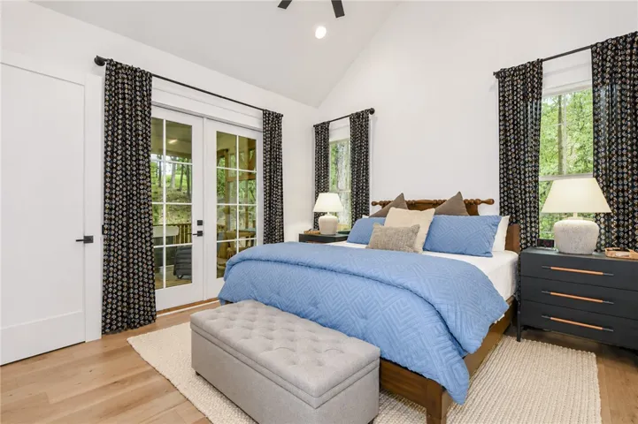 Hardwood floors and a vaulted ceiling elevate this primary bedroom, offering direct outdoor access through French doors.