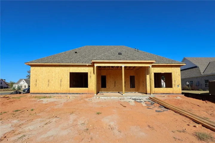 A new construction home features a covered back porch and a shingle roof under clear blue skies.