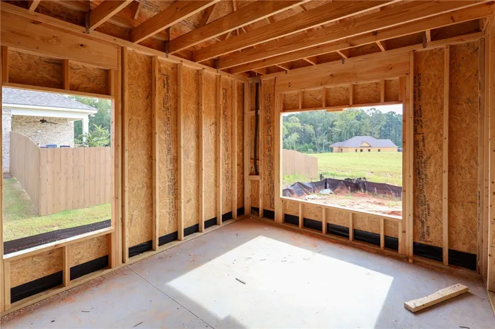 Exposed wood framing and concrete flooring outline a future living space with large window openings.