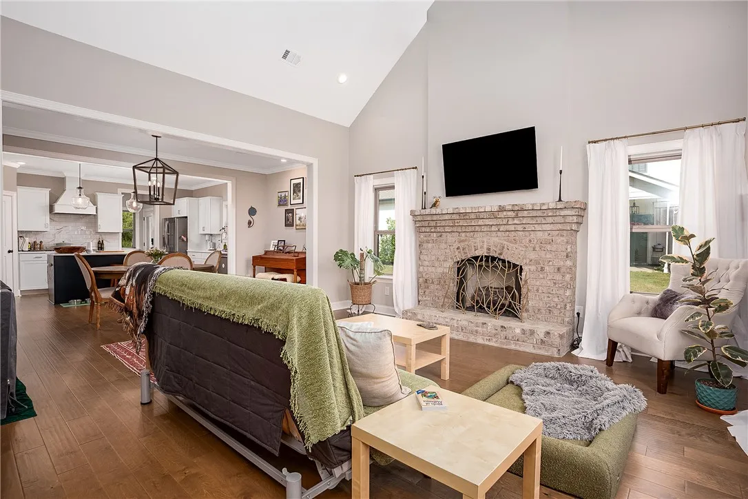 A well-lit living space features soaring ceilings, a traditional brick fireplace, and rich hardwood flooring.