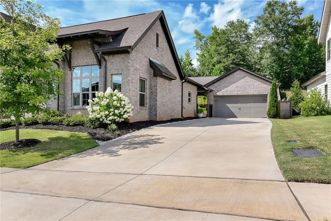 An inviting light-brick facade with a neatly landscaped front yard leads to a spacious concrete driveway and attached garage.
