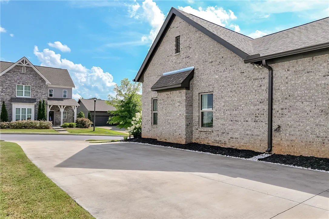 A grand, grey-brick residence with a spacious concrete driveway under a dynamic sky.