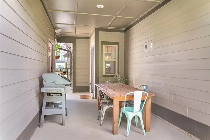 An inviting covered patio, perfect for alfresco dining, features plank siding and a sturdy wooden table.