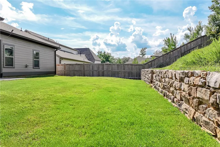 A spacious backyard with vibrant green grass, secured by a stone retaining wall and privacy fence.