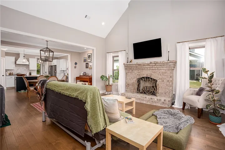 A well-lit living space features soaring ceilings, a traditional brick fireplace, and rich hardwood flooring.