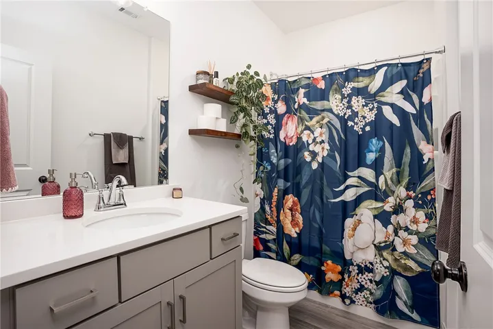 A well-appointed bath features stylish floating shelves and a captivating floral shower curtain.
