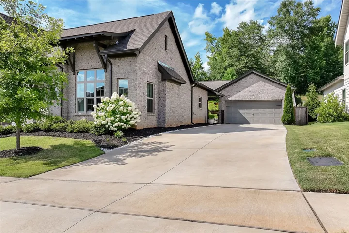 An inviting light-brick facade with a neatly landscaped front yard leads to a spacious concrete driveway and attached garage.