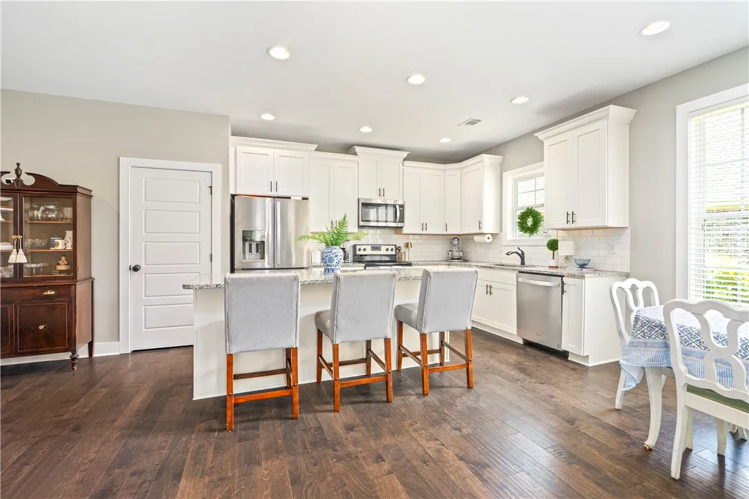 A luminous kitchen features white cabinetry, granite countertops, and wood flooring, creating an inviting space to gather for meals.