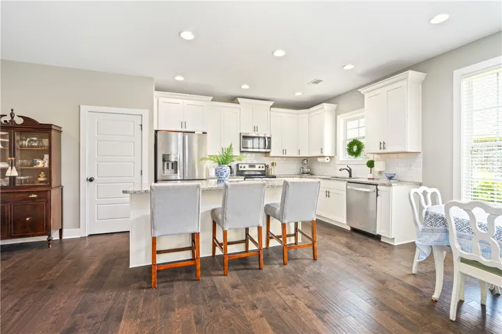 A luminous kitchen features white cabinetry, granite countertops, and wood flooring, creating an inviting space to gather for meals.
