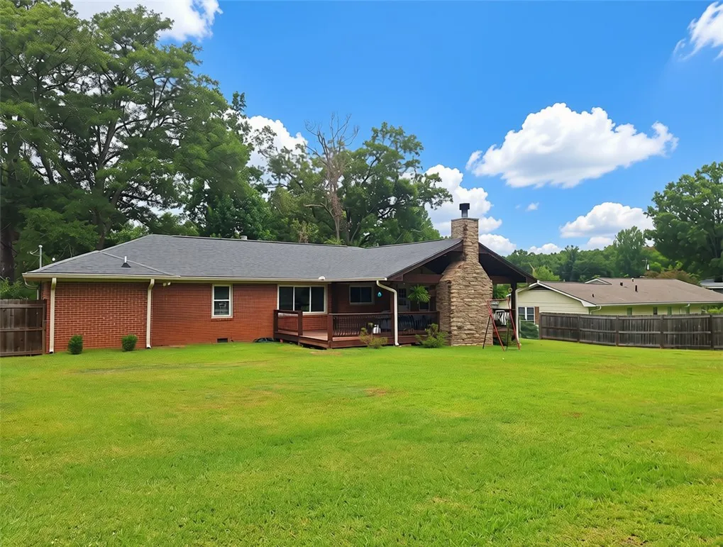 A spacious backyard with mature trees, a wooden deck, and a classic brick and stone home.