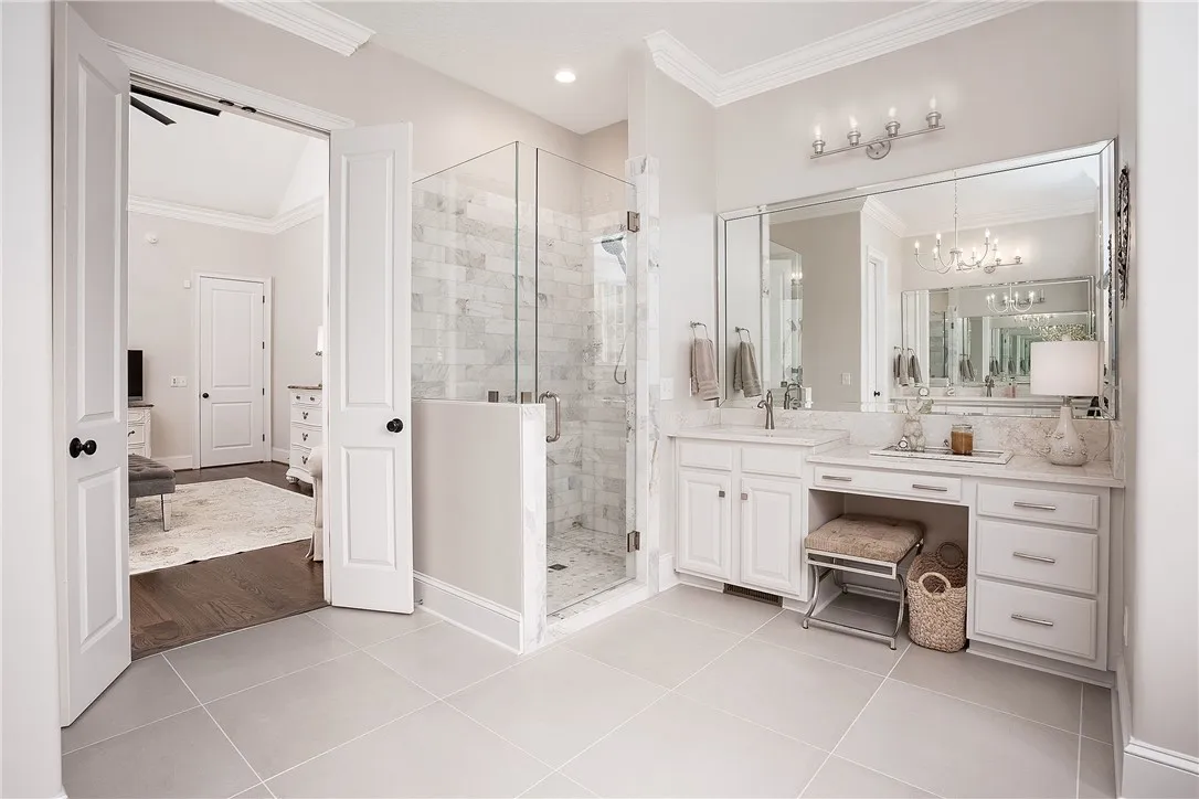 Marble accents and crown molding elevate this master bathroom, featuring a glass-enclosed shower and dual vanity.