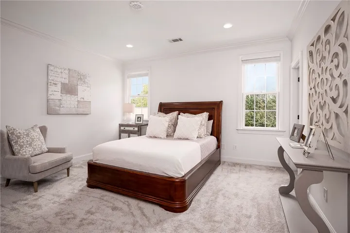 Recessed lighting and ample windows illuminate this comfortable bedroom, featuring soft carpeting and elegant crown molding.