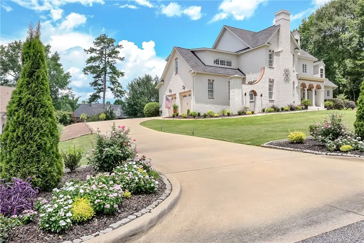 A graceful circular drive leads to a striking, meticulously landscaped estate with elegant brickwork and arched accents.