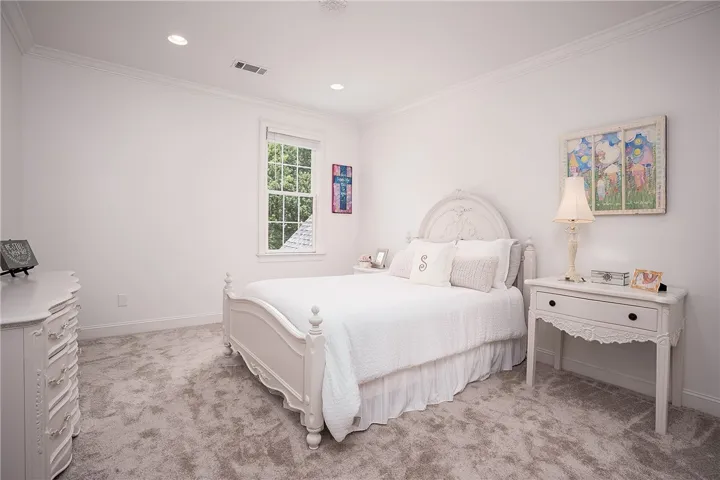 Recessed lighting illuminates this tranquil bedroom with plush carpet and ample natural light from a window.