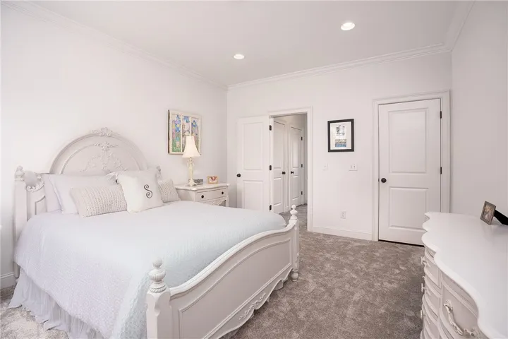 Recessed lighting illuminates a comfortable bedroom, featuring soft carpeting and elegant crown molding.