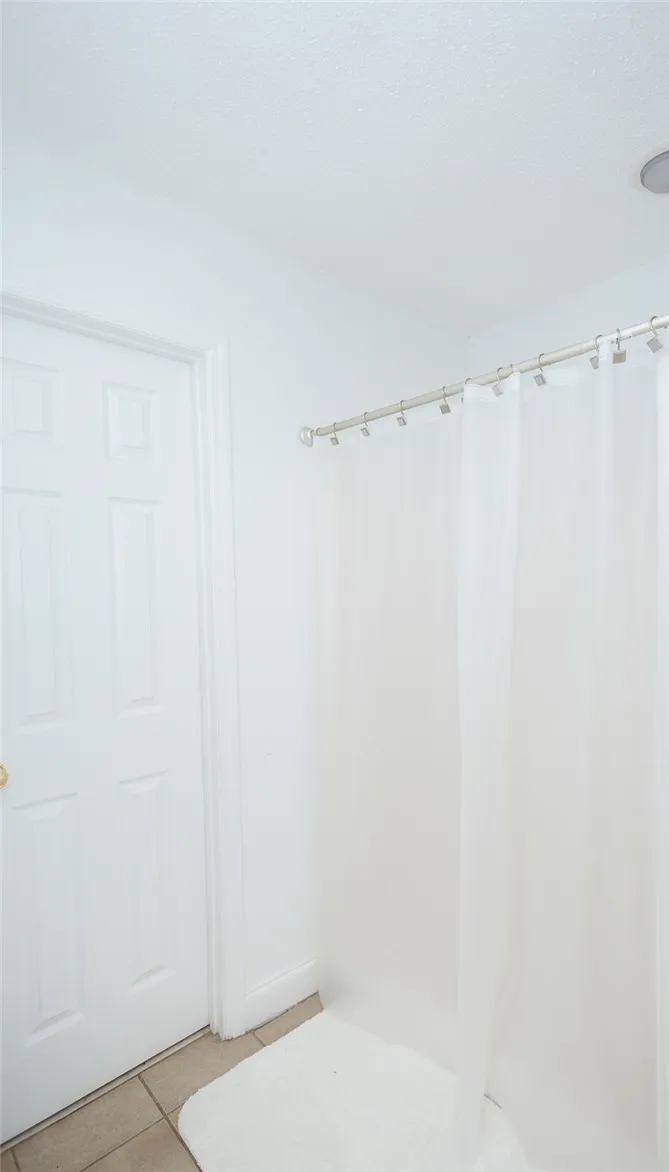 Functional full bathroom featuring a tub with a simple shower curtain and tiled floor.