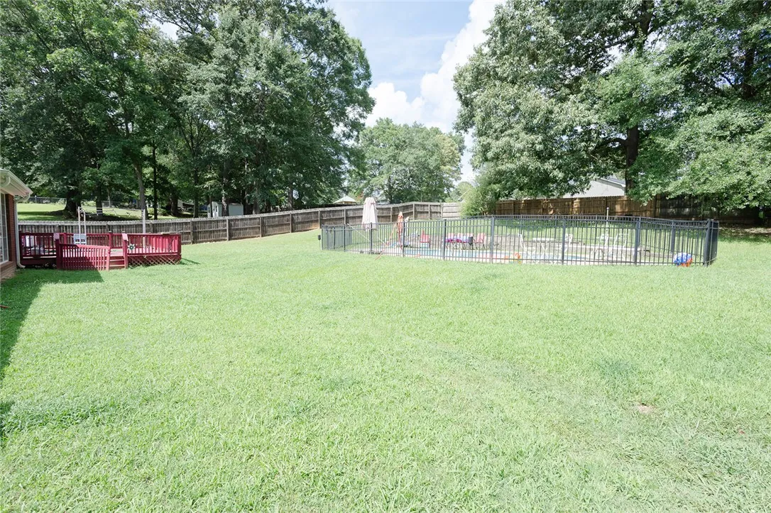 A spacious backyard retreat features a privacy fence, a wooden deck, and a fenced-in swimming pool.